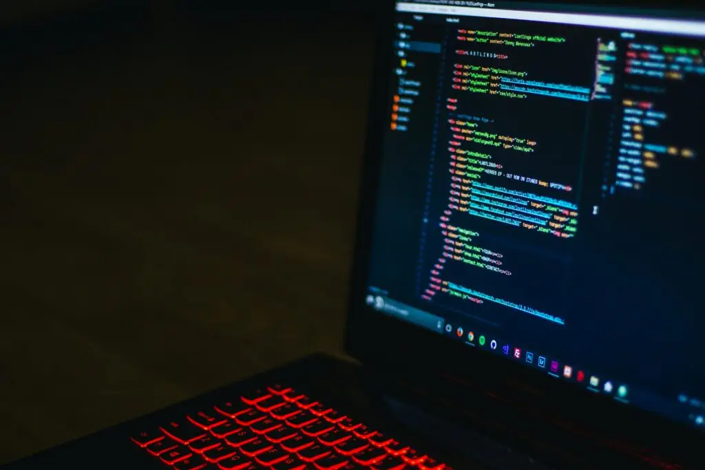 Dark-themed laptop with red backlit keyboard and HTML code on screen, showcasing the advanced web development and bespoke tech solutions offered by Rebellion Websites